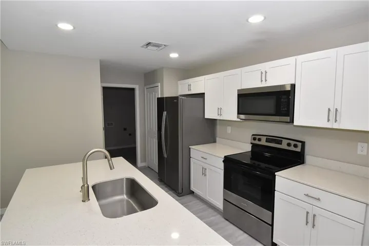 Kitchen with appliances with stainless steel finishes, white cabinetry, light stone countertops, recessed lighting, and light wood-style flooring