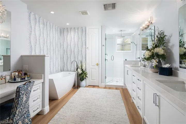Bathroom featuring a stall shower, a soaking tub, wood finished floors, double vanity, and recessed lighting