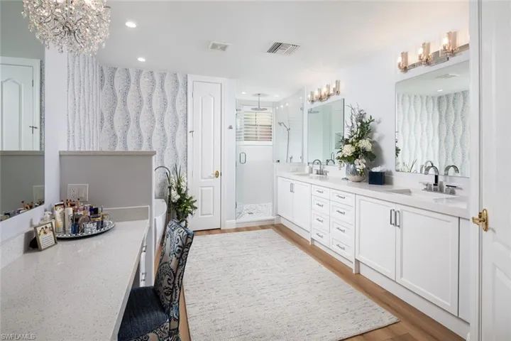 Full bath featuring a shower stall, double vanity, a chandelier, wood finished floors, and a bath