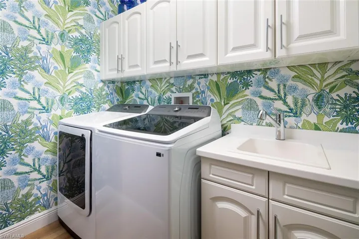 Laundry area with cabinet space, washer and dryer, laundry sink and wallpapered walls