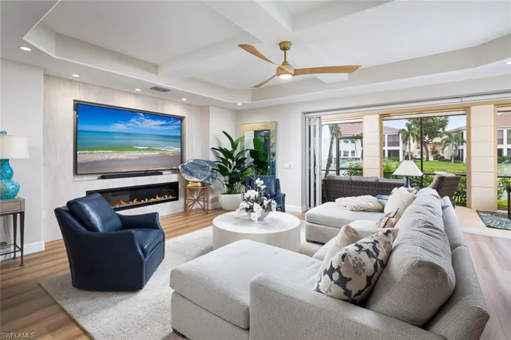 Living area featuring coffered ceiling, a glass covered fireplace, wood finished floors, recessed lighting, and a ceiling fan