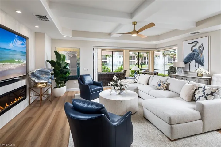 Living area featuring wood finished floors, a fireplace, ceiling fan, beam ceiling, and coffered ceiling