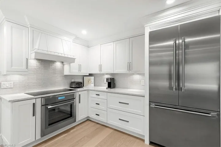 Kitchen with appliances with stainless steel finishes, white cabinets, custom range hood, light wood finished floors, and recessed lighting