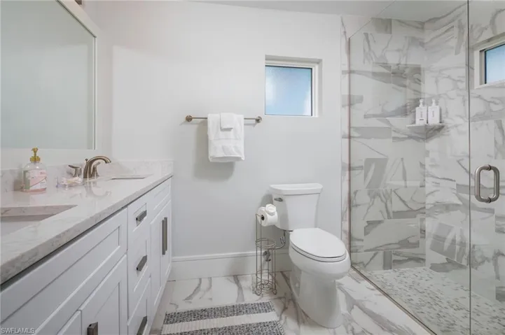 Bathroom with double vanity, light marble finish floors, and a marble finish shower