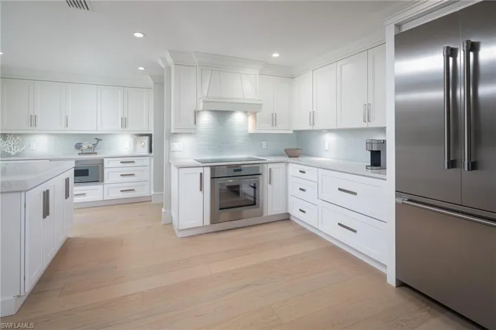 Kitchen with appliances with stainless steel finishes, white cabinets, custom range hood, light wood-style floors, and recessed lighting
