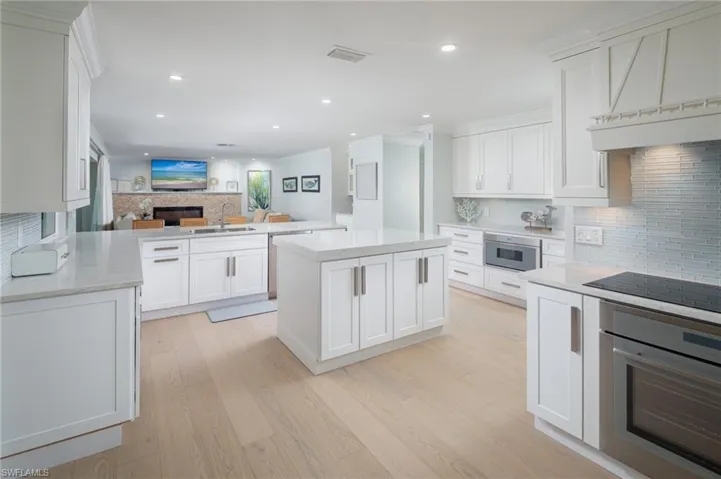Kitchen with decorative backsplash, white cabinets, wall oven, open floor plan, and a center island