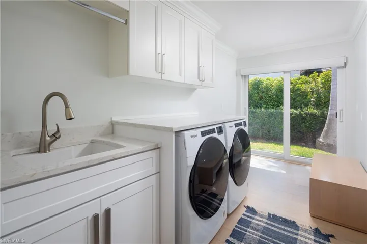 Laundry area with cabinet space, light wood-style flooring, washing machine and dryer, and ornamental molding