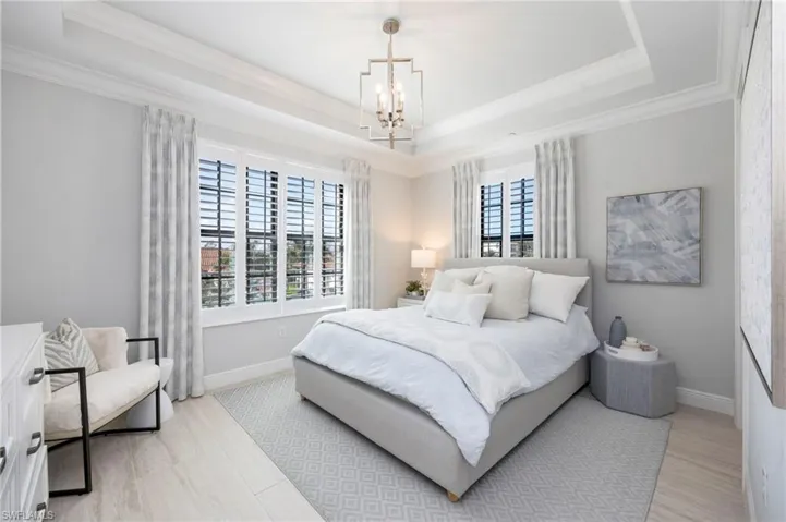 Bedroom with suspended lighting, a raised ceiling, and light wood-style flooring