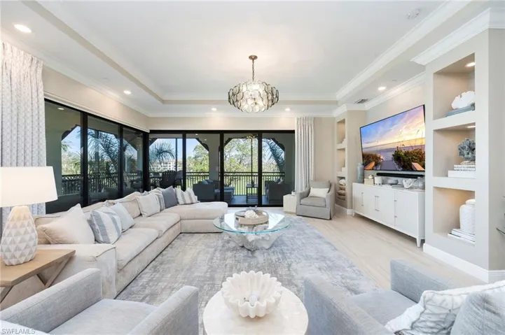 Living room with built in shelves, a chandelier, a tray ceiling, crown molding, and light wood-style floors