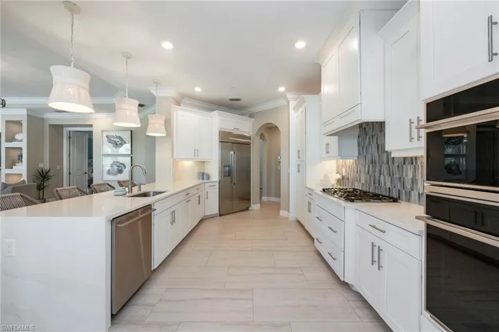 Kitchen featuring arched walkways, light stone counters, stainless steel appliances, a peninsula, and ornamental molding