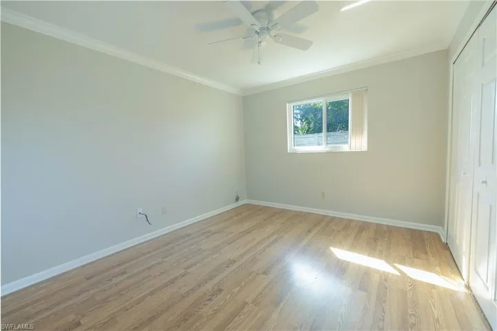Unfurnished bedroom featuring light wood-type flooring, a closet, baseboards, crown molding, and ceiling fan