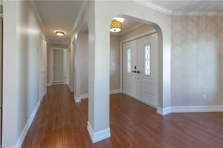 Foyer featuring arched walkways, ornamental molding, baseboards, and dark wood-style floors