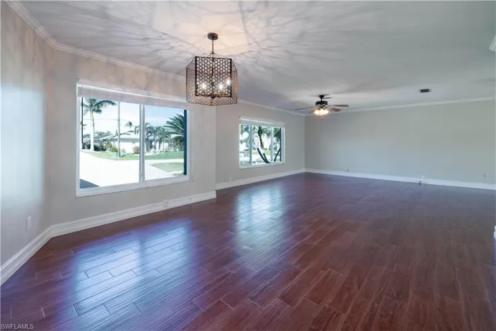 Unfurnished living room with dark wood-style flooring, baseboards, ornamental molding, visible vents, and ceiling fan with notable chandelier