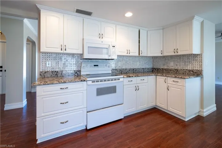Kitchen with white appliances, visible vents, baseboards, and dark wood finished floors