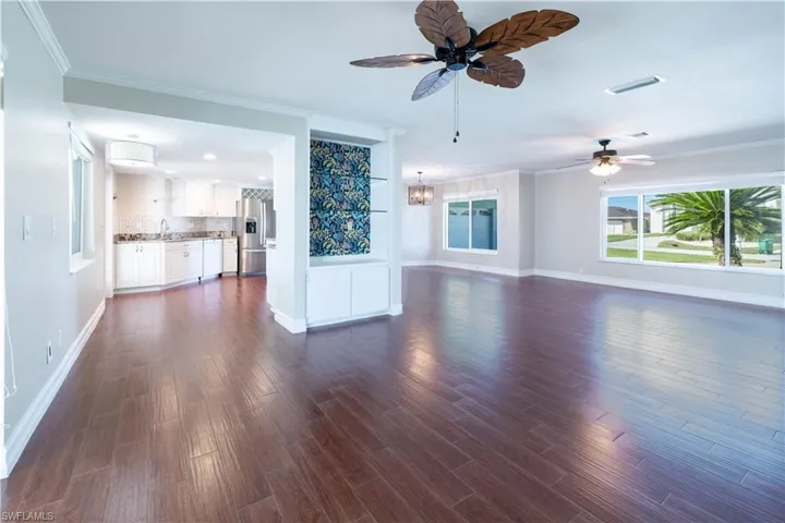 Unfurnished living room featuring dark wood-style flooring, baseboards, crown molding, visible vents, and ceiling fan