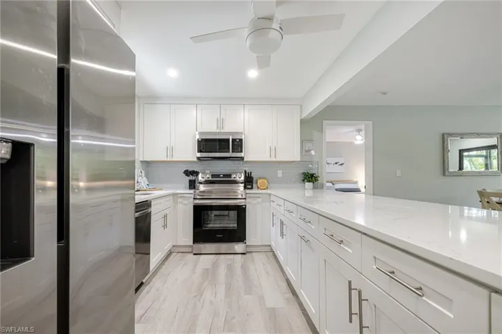 Kitchen featuring stainless steel appliances, white cabinetry, light stone counters, ceiling fan, and recessed lighting