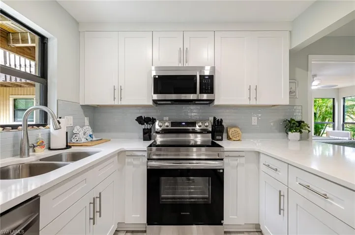 Kitchen featuring stainless steel appliances, white cabinets, light stone countertops, and backsplash
