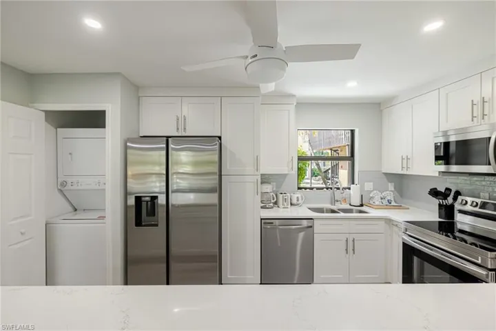 Kitchen with stainless steel appliances, white cabinets, light stone countertops, stacked washer / drying machine, and recessed lighting