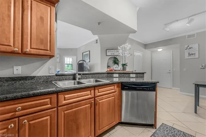 Kitchen with dishwasher, ornamental molding, light tile patterned floors, brown cabinetry, and dark stone counters