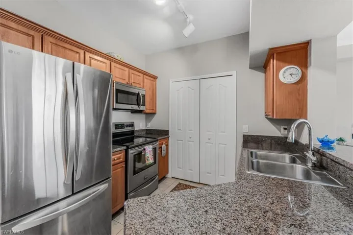 Kitchen featuring stainless steel appliances, light tile patterned floors, rail lighting, brown cabinets, and dark stone counters