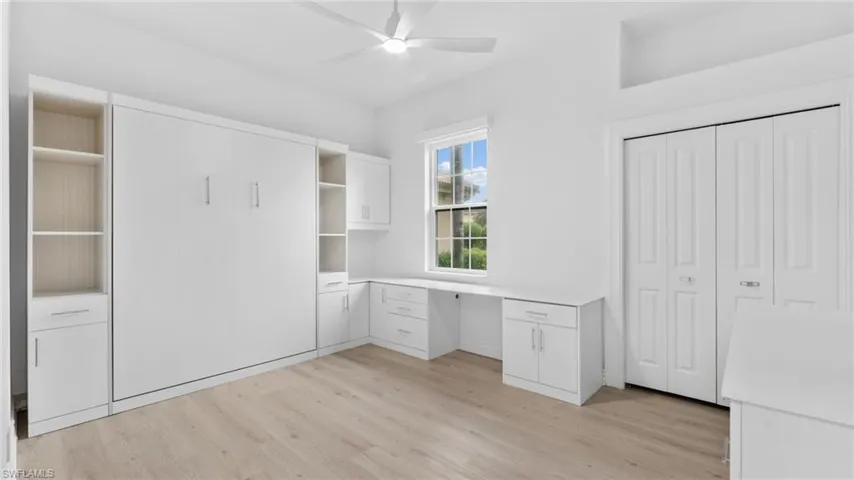 Unfurnished office featuring light wood-type flooring, built in desk, and ceiling fan