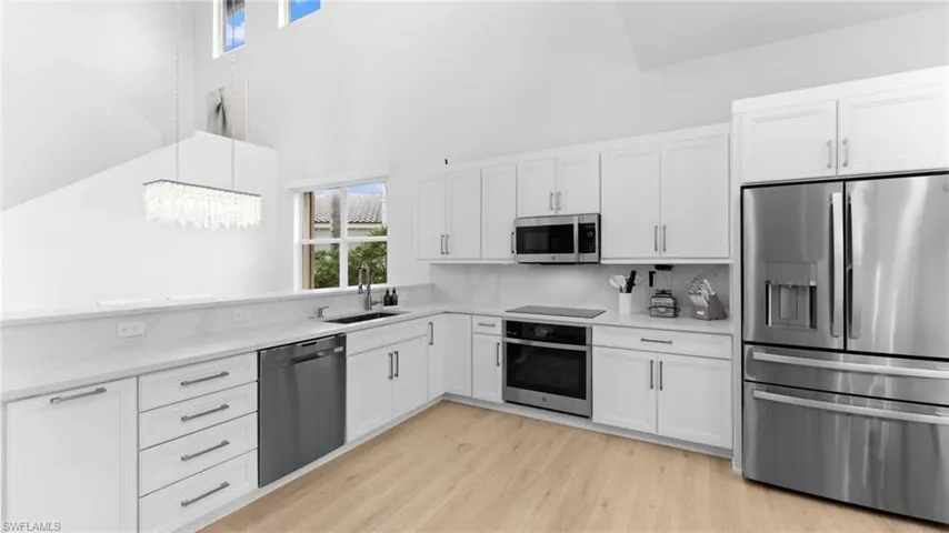 Kitchen with white cabinets, hanging light fixtures, sink, and appliances with stainless steel finishes