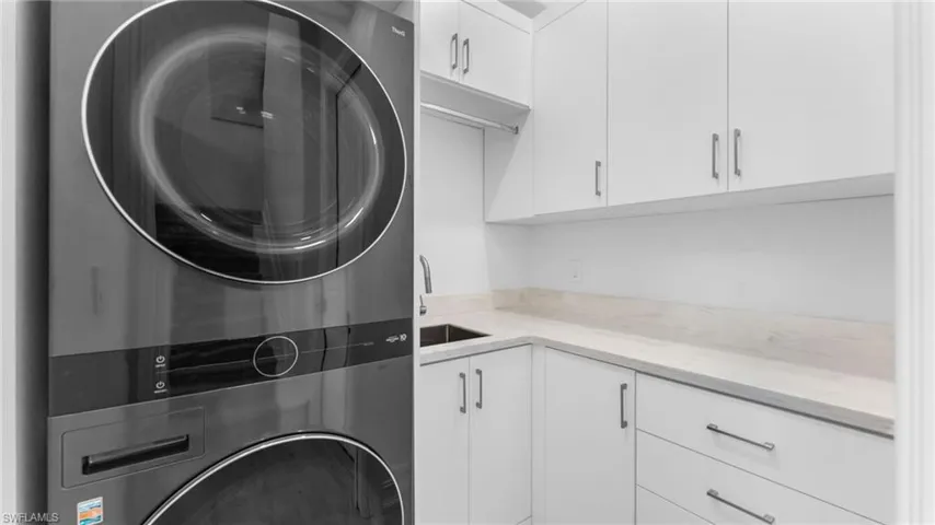 Washroom featuring cabinets, stacked washing maching and dryer, and sink