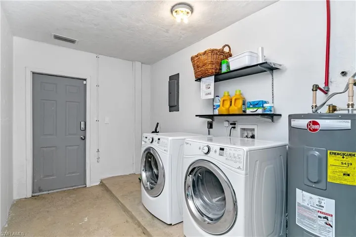 Laundry area featuring electric water heater, unfinished concrete flooring, a textured ceiling, washer and clothes dryer, and electric panel