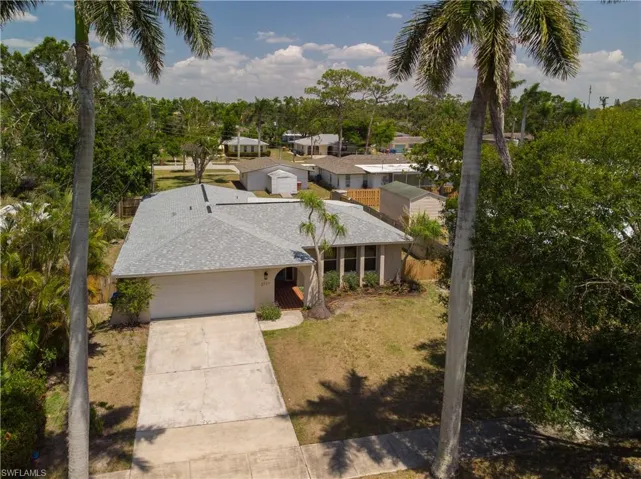 View of front of home with concrete driveway, a garage, roof with shingles, and view of wooded area