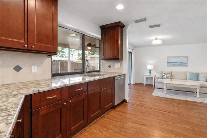 Kitchen with light stone countertops, open floor plan, light wood finished floors, dishwasher, and backsplash