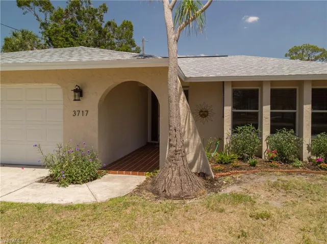 Property entrance featuring stucco siding, a shingled roof, a garage, and a yard