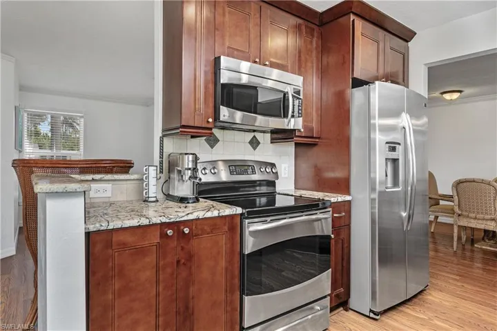 Kitchen featuring stainless steel appliances, ornamental molding, light wood finished floors, light stone counters, and tasteful backsplash