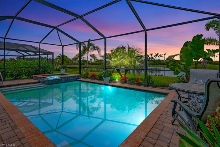 Pool at dusk featuring an in ground hot tub, glass enclosure, and a patio area
