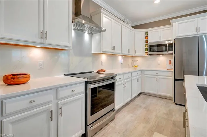 Kitchen with appliances with stainless steel finishes, white cabinets, decorative backsplash, and wall chimney range hood