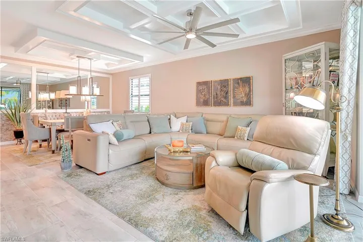 Living room with coffered ceiling, ornamental molding, ceiling fan with notable chandelier, and light tile patterned floors