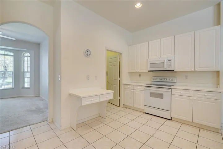 Kitchen with white cabinets, white appliances, and light tile floors