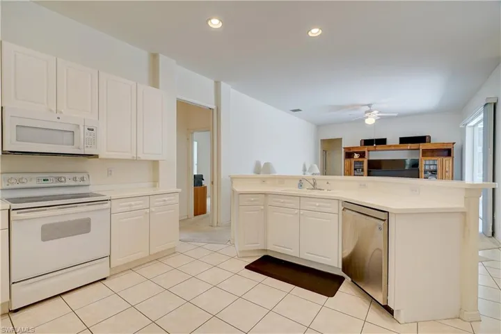 Kitchen with white appliances, white cabinetry, ceiling fan, and light tile floors