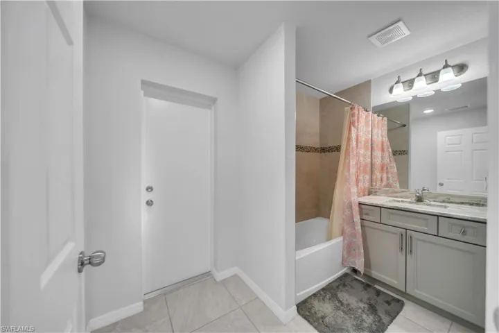 Full bath featuring vanity, shower / bathtub combination with curtain, and light tile patterned flooring