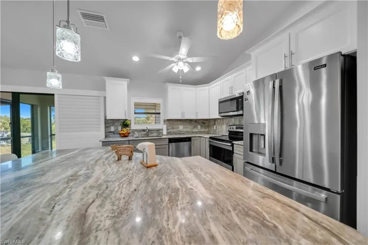 Kitchen featuring stainless steel appliances, pendant lighting, light stone counters, a ceiling fan, and decorative backsplash