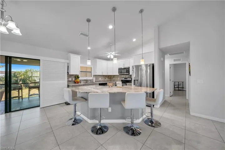 Kitchen featuring a center island, white cabinetry, light stone counters, a kitchen breakfast bar, and vaulted ceiling