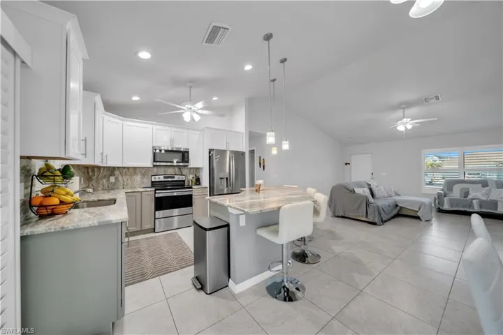 Kitchen featuring a ceiling fan, stainless steel appliances, a kitchen breakfast bar, light stone countertops, and vaulted ceiling