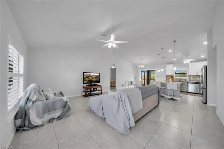 Living room featuring a ceiling fan, lofted ceiling, and light tile patterned flooring