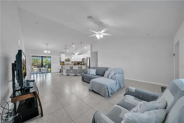Living room with hanging lights, a ceiling fan, light tile patterned flooring, and lofted ceiling