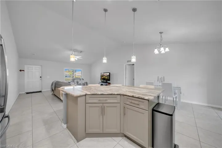 Kitchen with a kitchen island, lofted ceiling, light stone counters, open floor plan, and gray cabinetry