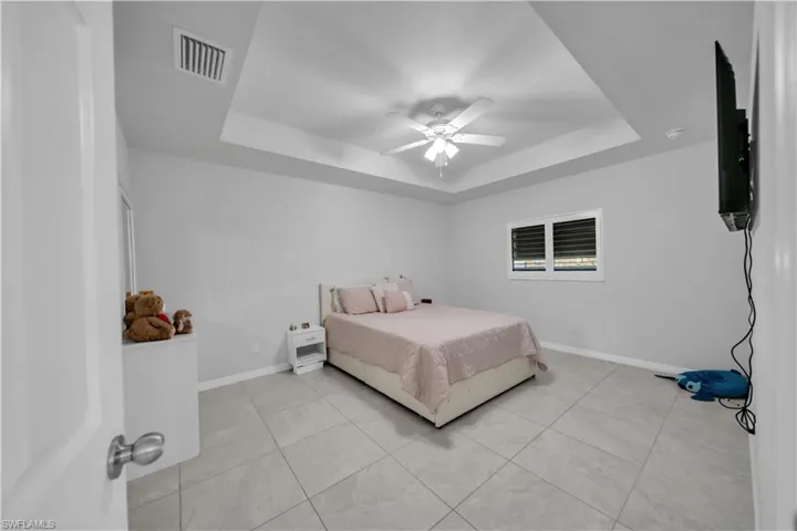 Bedroom with a tray ceiling, ceiling fan, and light tile patterned floors