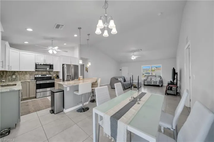Dining room featuring a ceiling fan, a chandelier, light tile patterned floors, and vaulted ceiling