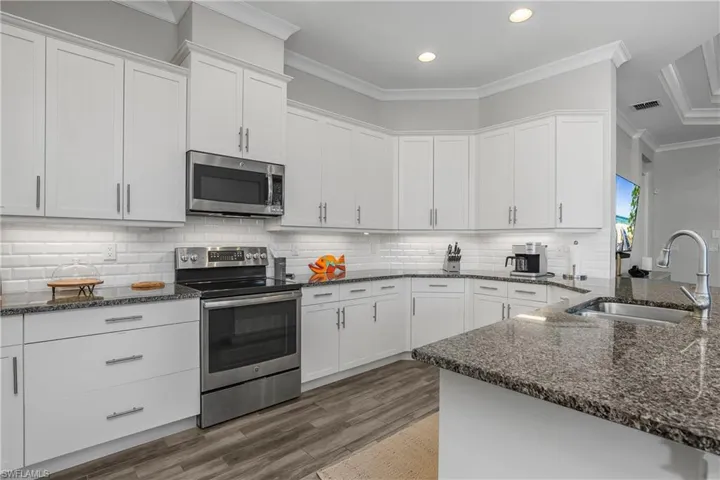Kitchen with stainless steel appliances, white cabinetry, dark stone counters, crown molding, and backsplash