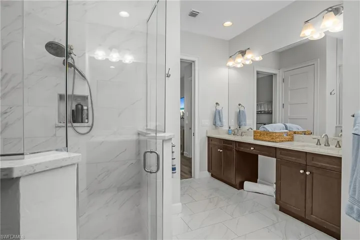 Owner's Bathroom with double vanity, a marble finish shower, light marble finish floors, and recessed lighting