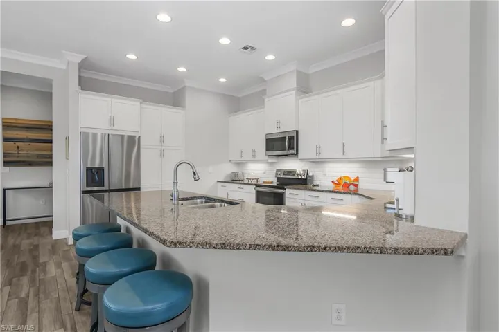 Kitchen featuring stone countertops, stainless steel appliances, white cabinets, a peninsula, and tasteful subway tile backsplash.