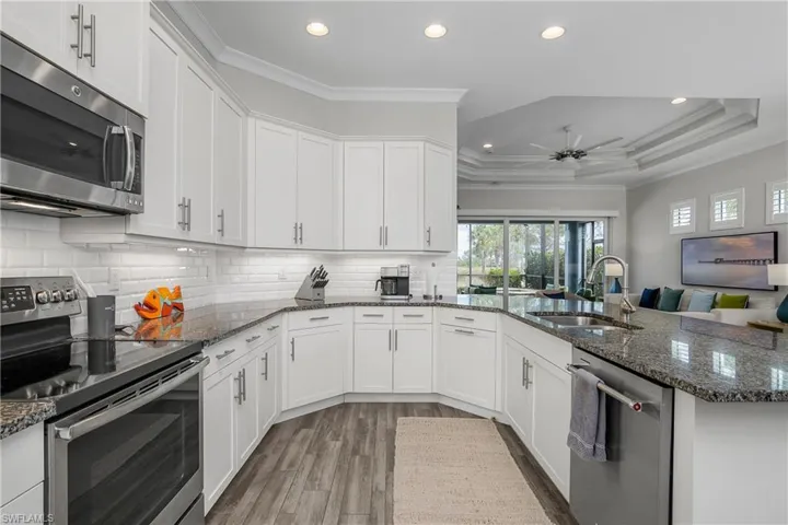 Kitchen featuring stainless steel appliances, crown molding, white cabinetry, dark stone counters, and a peninsula